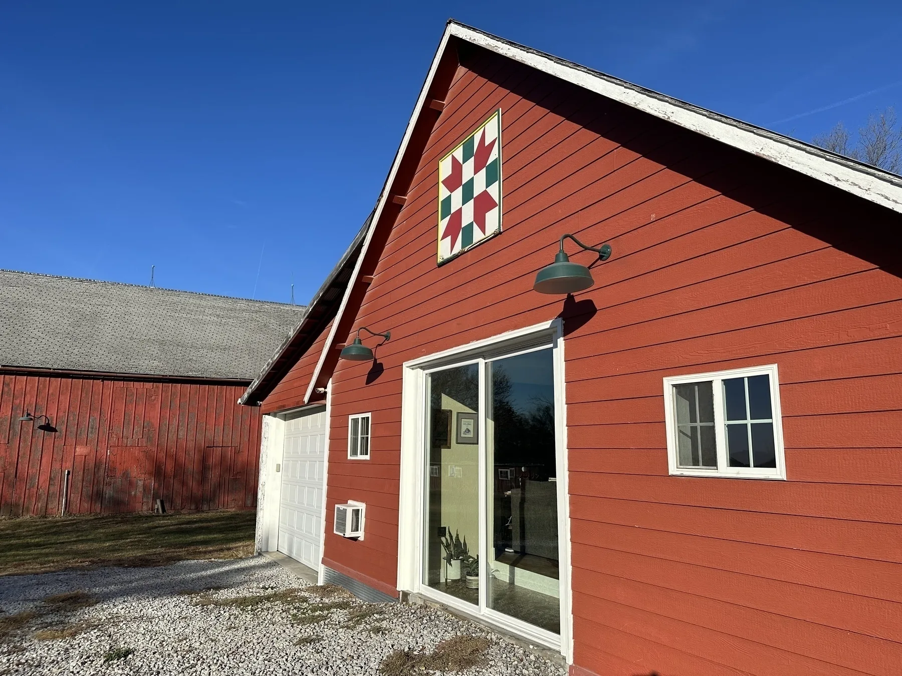 A red barn with a geometric quilt pattern and outdoor lights is set against a clear blue sky.