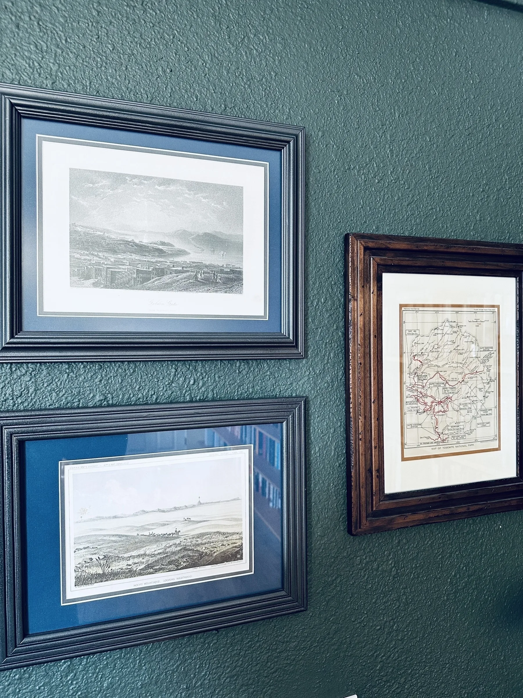 Three framed pictures hang on a green wall, featuring landscapes and a vintage map.