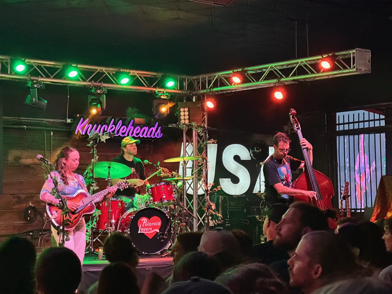 A band is performing on stage at a venue with colorful lighting and a lively audience.