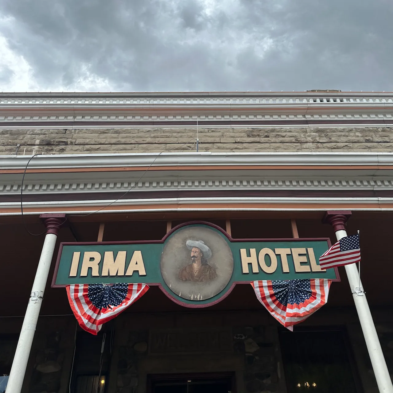 A historic hotel entrance features a prominent sign reading IRMA HOTEL with decorative bunting and a circular portrait above.