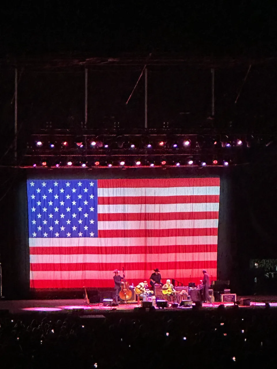 A stage features musicians performing in front of a large American flag backdrop.