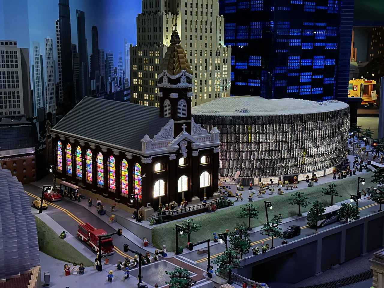 A detailed LEGO cityscape features a church with colorful stained glass windows, surrounded by skyscrapers and lively street scenes.