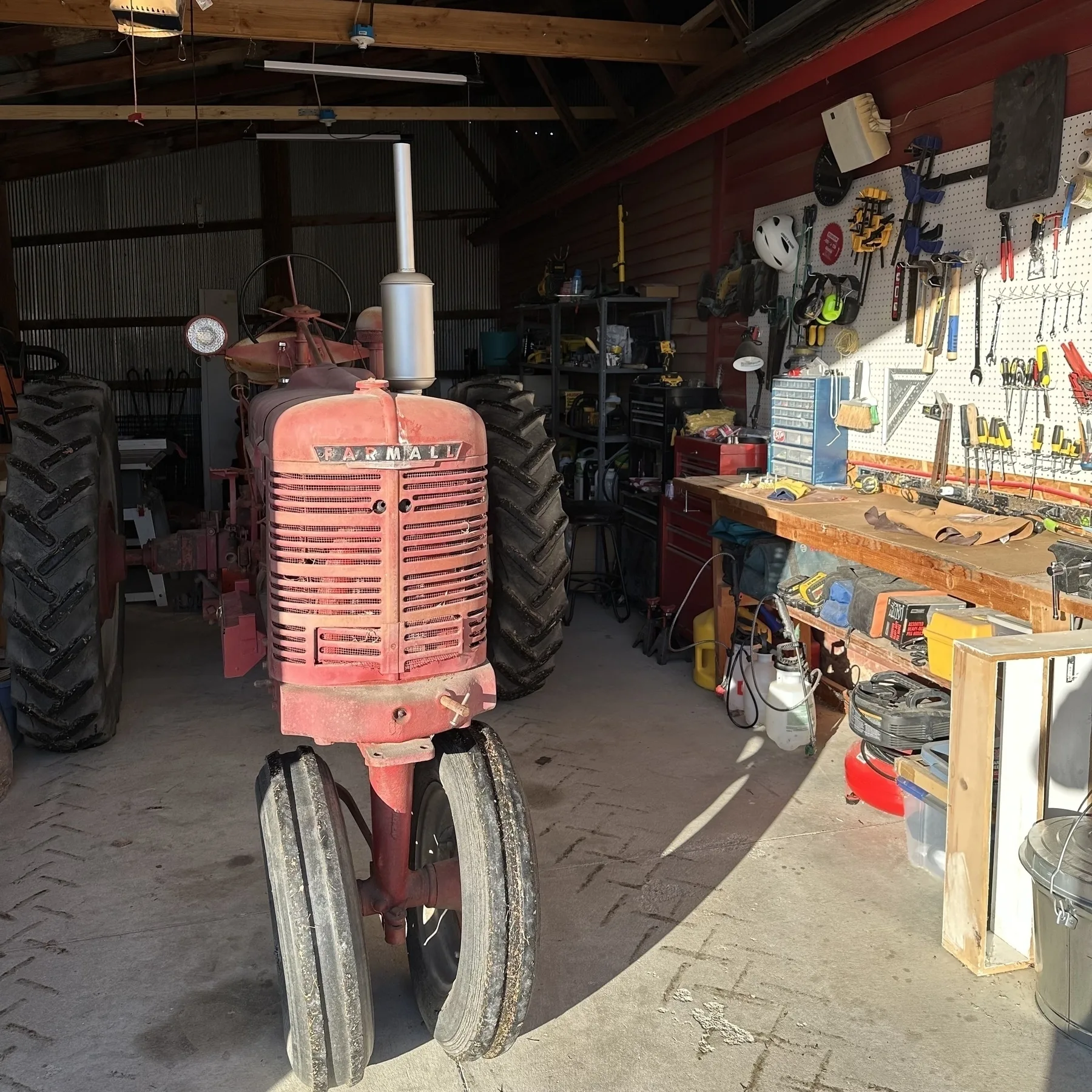 A red tractor is parked inside a well-organized garage with various tools and equipment on the walls and workbench.
