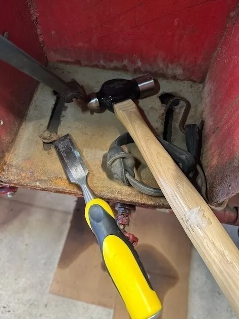 A hammer and a chisel with a yellow handle are placed inside a rusty metal container along with some coiled wires.