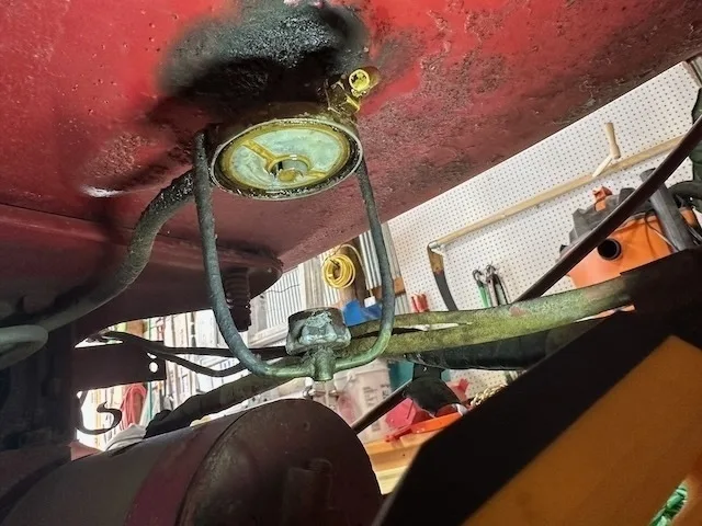 Underneath the vehicle, there is a circular metal component attached with supports and surrounded by pipes and tubing, indicating part of an automotive system.