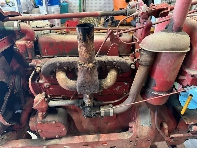An old, worn-out engine with rusted parts and red paint is displayed in a workshop setting.