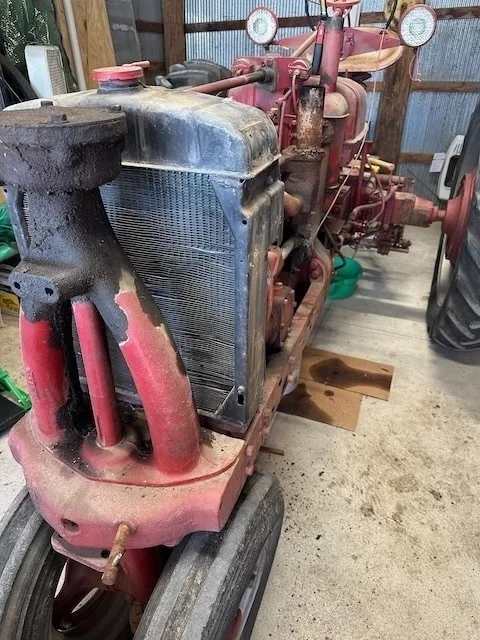 A vintage red tractor with worn paint is parked inside a corrugated metal shed.