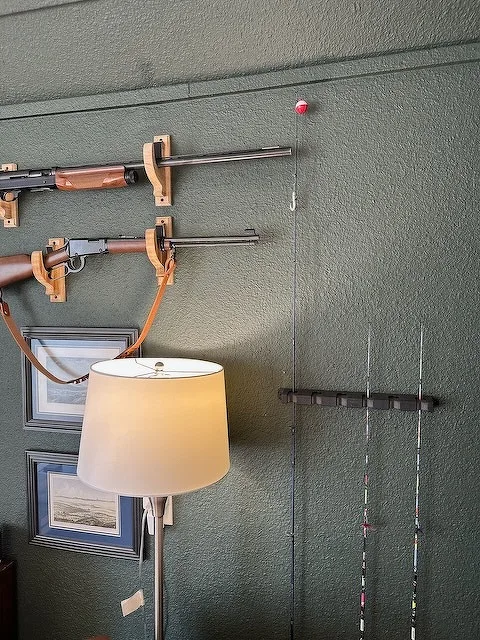 A wall-mounted display features rifles and fishing rods, alongside framed pictures and a floor lamp.