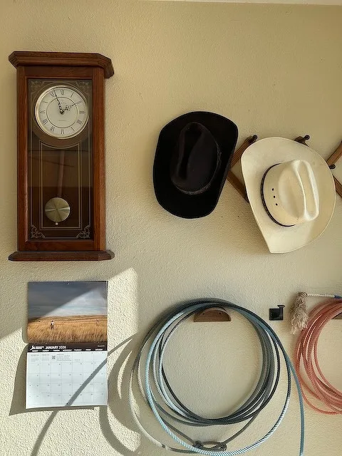A wall display features a wooden clock, two cowboy hats, a calendar, and several coiled ropes.